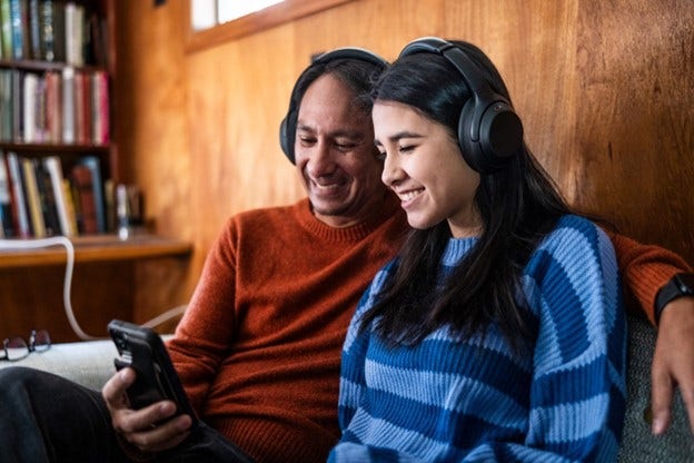 a father and daughter watching a smartphone with headphones on